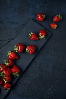 Lacivert arka planda siyah servis tahtasıyla olgun kırmızı çilekler. Masadaki taze böğürtlenlerden tatlı. Üst Manzara. Metin için boşluk.