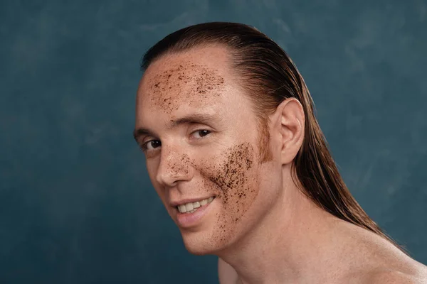 Smiling man with wet long hair in coffee mask on his face waiting of the spa procedures.