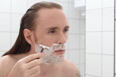 Banyodaki aynanın önünde yüzünü tıraş eden uzun saçlı özenli bir adam.. 