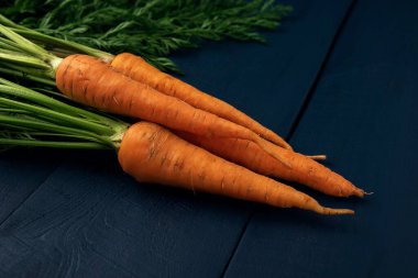 Tahta bir masada yeşil yapraklı bir avuç çiğ havuç. Koyu arkaplanda taze sebzeler.