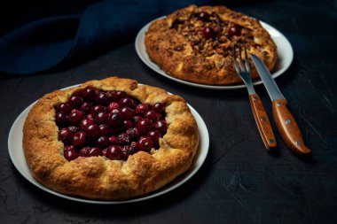 Koyu kırmızı kiraz ve lacivert arka planda ceviz dolu iki galon. Peçete ve çatal bıçaklı ev yapımı tatlı turta.. 