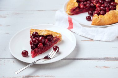 Olgun kırmızı kiraz dolgulu bir galet ve beyaz tabakta tatlı çatalı. Provence tarzı ahşap arka planda ev yapımı tatlı turta. 