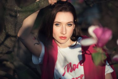 Manolya ağacına poz veren çekici genç bir kadın. Pembe çiçekli güzel moda kızı..