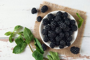 Böğürtlenli beyaz tabak ve çuval bezi yapraklı ve beyaz Provence tarzı ahşap masa. Düz yatıyordu. Boşluğu kopyala.