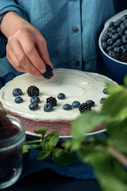 Kadın eli süzme peynirli güvecin üzerine böğürtlen koydu. Kadın süzme peynirli turtayı böğürtlenlerle süslüyor.. 