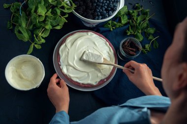 Kadın elleri süzme peynir güvecine ekşi krema sürer. Kremalı süzme peynirli turtayı dekore eden kadın. Üst görünüm.