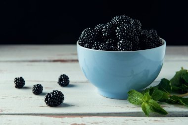 Beyaz Provence tarzı ahşap masada olgun böğürtlen ve nane yapraklarıyla kase. 