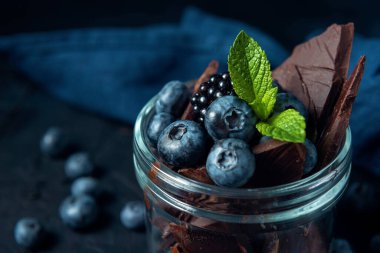 Koyu dokulu arka planda yabanmersini, böğürtlen, nane ve çikolata parçalarıyla yakın çekim kavanozu.. 