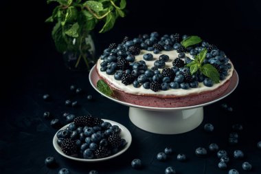 Koyu arkaplanda böğürtlen ve yabanmersinli süzme peynir turtası ve tabak. 