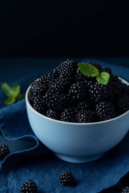 Olgun böğürtlenli kase ve siyah ahşap masada nane yaprakları. 