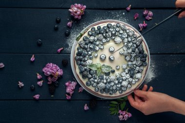 Koyu ahşap masada böğürtlen, yabanmersini ve akasya çiçekleriyle süslenmiş süzme peynir güveci. Düz yatıyordu. Boşluğu kopyala.