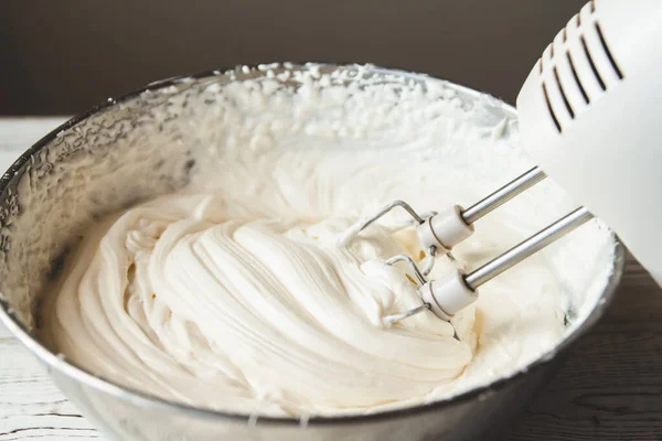 White butter cream in a metal bowl. Beating cream cake. Mixer whisk in cream.