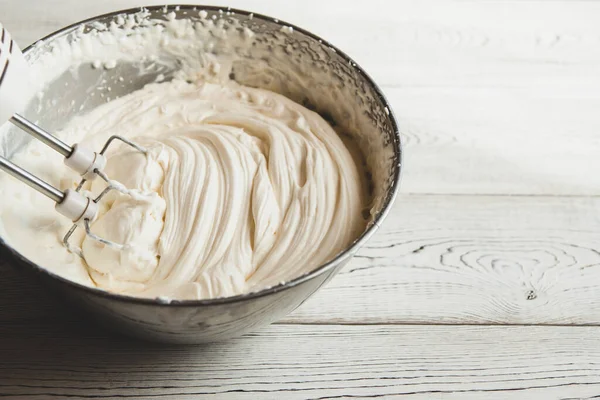 White butter cream in a metal bowl. Beating cream cake. Mixer whisk in cream.