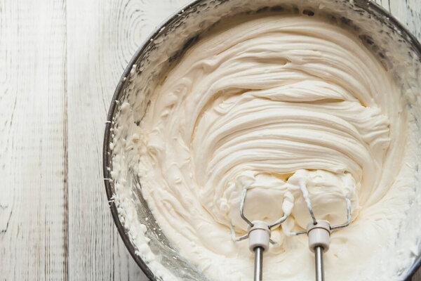 White butter cream in a metal bowl. Beating cream cake. Mixer whisk in cream.