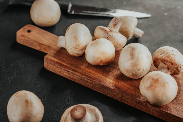 Fresh champignons on a wooden board. Slicing mushrooms.