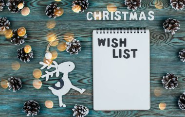 Not defteri ve ahşap harflerle çevrili koniler ve mavi ahşap arka plan fotokopi alanı üzerinde noel oyuncakları. Noel dilek listesi.