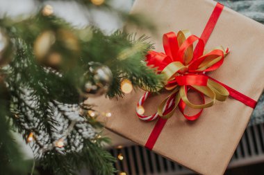 Kırmızı ve yeşil fiyonklu bir hediye kutusu Noel ağacının yanındaki pencere eşiğinde duruyor..