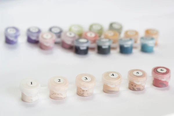 Small colored paint jars. Numbered by numbers. Close-up. On a light background. Place for an inscription. The background.