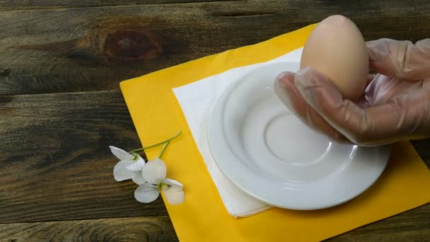 Человек берет вареное яйцо руками из белая тарелка, разбивает скорлупу чайной ложкой и очищает яйцо. Крупный план . — стоковое видео