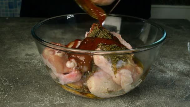 Chef prepares marinade and stirs raw chicken wings for barbecue or frying in deep glass bowl. Olive oil, spices, savory sauce are mixed with chicken meat. Close-up. — Stock Video