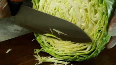 Şef, taze lahana ve mutfak bıçağını salata ya da diğer yemekleri hazırlamak için tahta kesme tahtasıyla ince ince doğradı. Yakın plan. Kapalı.
