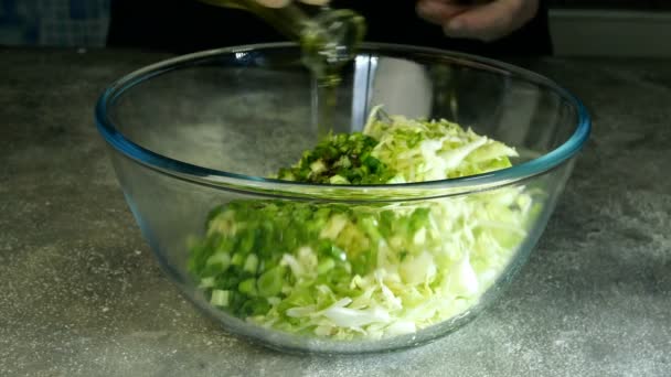 Kock häller matolja eller olivolja i genomskinlig glasskål med hackad kål och grön lök och blandar noggrant med spatel för att tillaga vegetarisk sallad eller annan maträtt. Närbild. — Stockvideo