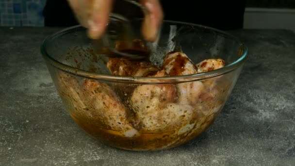 Chef prepares marinade and stirs raw chicken wings for barbecue or frying in deep glass bowl. Olive oil, spices, savory sauce are mixed with chicken meat. — Stock Video