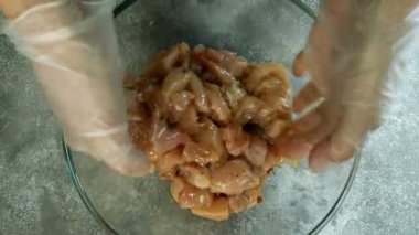 Şef çiğ tavuk göğsünü karıştırdı, küçük parçalara ayırdı, şeffaf cam bir kasede terbiye ve baharat ile elleriyle. Yukarıdan aşağıya yemek. Yukarıdan bak. Yakın plan. Makro.