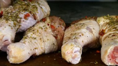 Baharat ve otlarla serpilmiş çiğ tavuk bacakları birbiri üzerine konur ve baharatlı sosla sulanır. Yakın plan. Makro.
