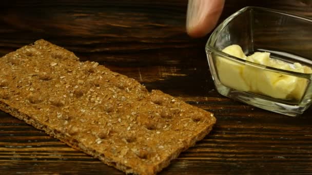 Chef-kok handen verspreiden boter op knäckebröd van transparante boterschaal, met keukenmes, besprenkeld zwarte gemalen peper. Close-up. — Stockvideo