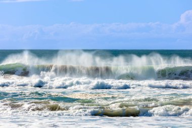 Photograph of waves from the Tasman Sea crashing onto Jones Beach against a blue sky near the town of Kiama Downs in the Illawarra region on the south coast of NSW, Australia.