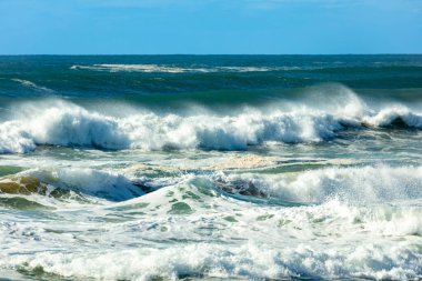 Photograph of waves from the Tasman Sea crashing onto Jones Beach against a blue sky near the town of Kiama Downs in the Illawarra region on the south coast of NSW, Australia.