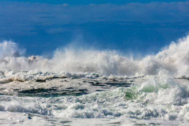 Photograph of waves from the Tasman Sea crashing onto Jones Beach against a blue sky near the town of Kiama Downs in the Illawarra region on the south coast of NSW, Australia.