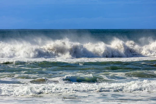Photograph of waves from the Tasman Sea crashing onto Jones Beach against a blue sky near the town of Kiama Downs in the Illawarra region on the south coast of NSW, Australia.