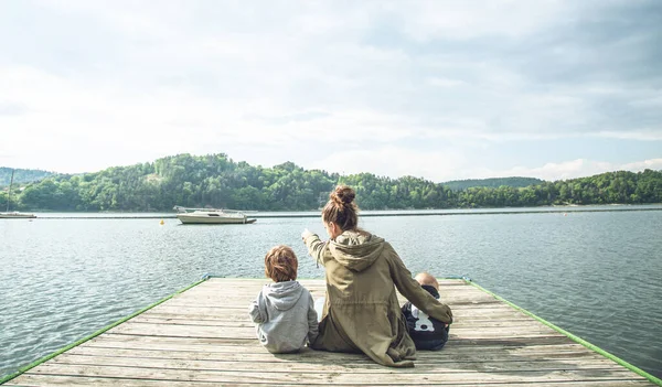 幸福的一家人坐在桥上 妈妈给孩子们看湖上的小船 从后面看 一家人去湖上旅行 图库图片