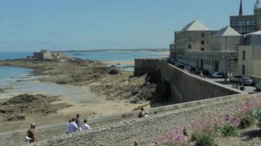 Saint Malo, Fransa Temmuz 2020. Şehir duvarlarından Fort Castle 'a deniz alçalınca turistler sahilde yürüyor.
