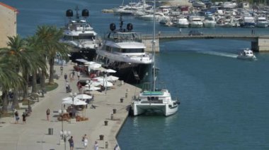 Trogir, Hırvatistan Eylül 2020. Dalmaçya 'nın Trogir kentindeki ana gezinti alanının tepesinden arka planda köprü araçları, turistler ve yelkenli gemiler görülüyor. 4K UHD