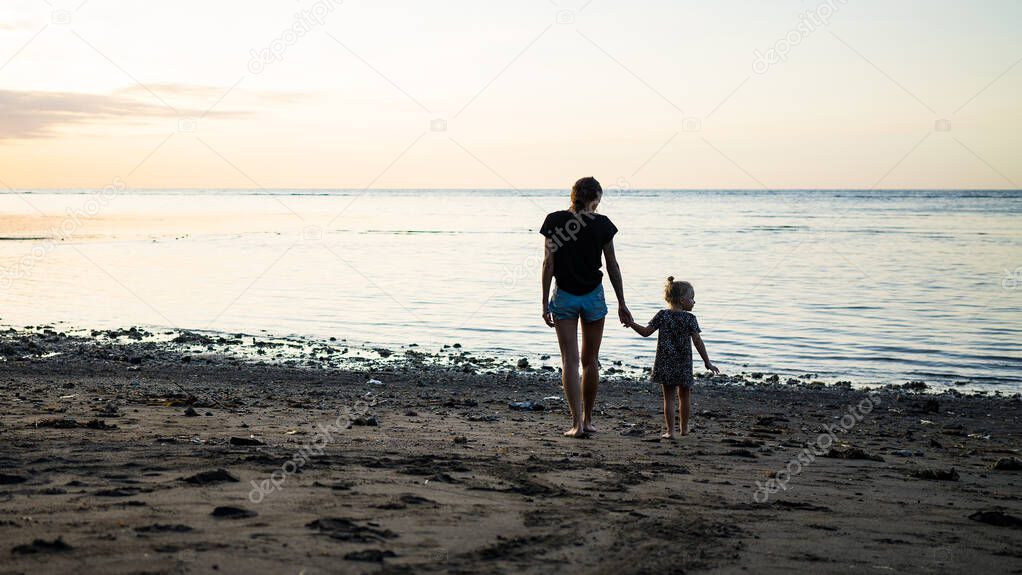 young mother and little kid walking on sandy beach 