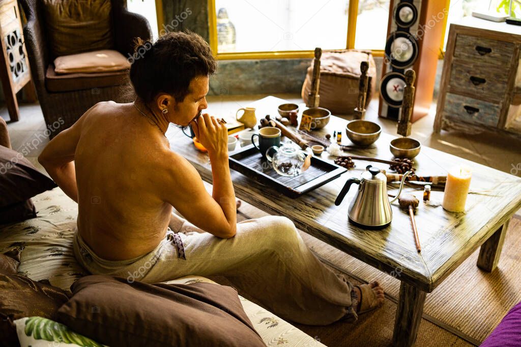 attractive man sitting on sofa and drinking tea on summer bungalow background