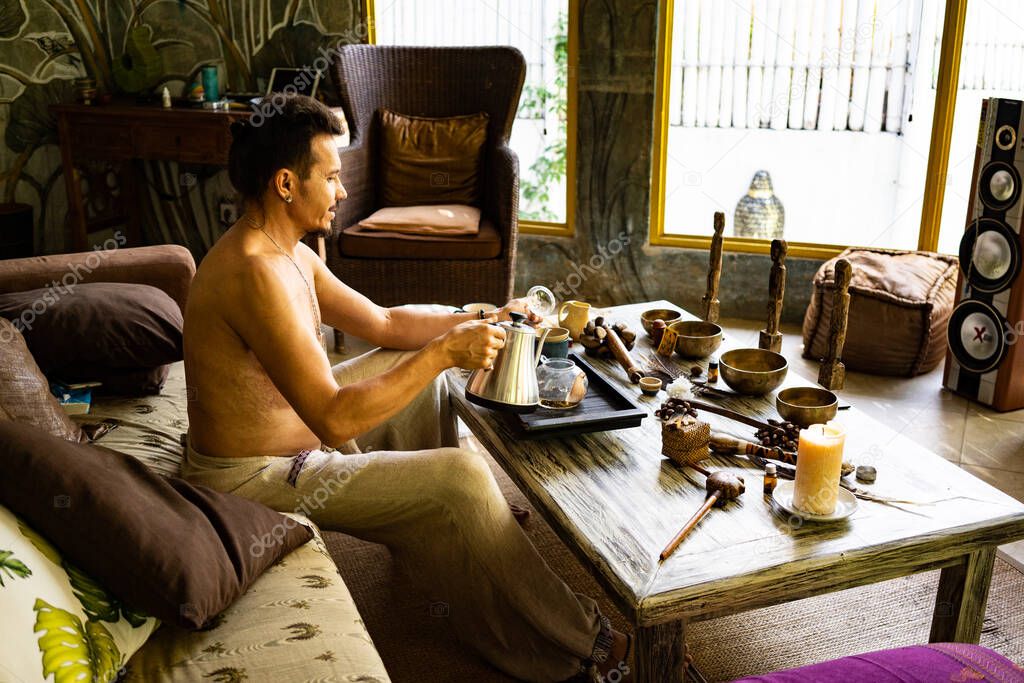 attractive man sitting on sofa and drinking tea on summer bungalow background