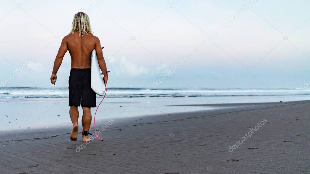 A surfer walking in from the water after a day out on the waves in Bali, Indonesia.