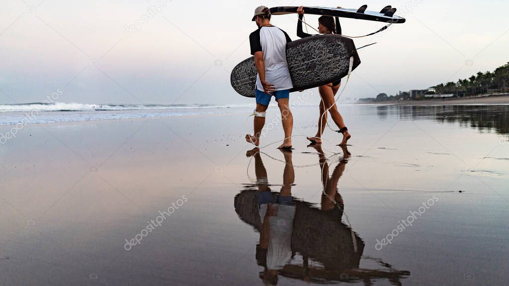 Young surfers walking on the beach in Bali, Indonesia.