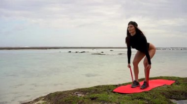 Mayolu genç bir kadın kumsalda egzersiz yapıyor. Doğanın ve fitness yaşam tarzının tadını çıkarıyor..