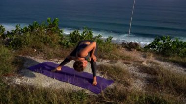 Genç kadın sabahları plajda yoga yapıyor.
