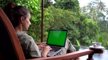 Yazlık villa arka planında yeşil ekranlı dizüstü bilgisayarla çalışan güzel bir kız.