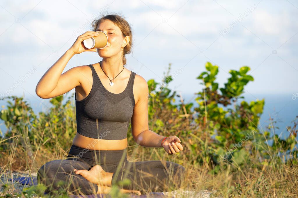 Amazing girl drinking morning coffee and practice yoga on the beach on mountains background