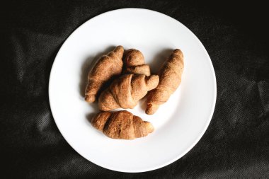 Siyah tekstil arka planında beyaz bir tabakta kruvasan. Taze fırın