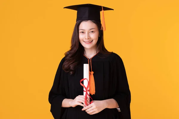 Happy Graduate asian woman in cap and gowm holding Certificated or diploma on yellow background,Summer Graduation Concept