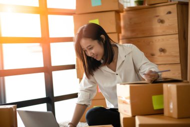 Evde online alışveriş için dizüstü bilgisayarla çalışan genç Asyalı kadınların KOBİ girişimcisi ve müşteriden istek ve sipariş, evde paketleme ve başlangıç konsepti ile Neşeli ve Mutlu