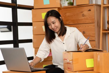 Evde online alışveriş için dizüstü bilgisayarla çalışan genç Asyalı kadınların KOBİ girişimcisi ve müşteriden istek ve sipariş, evde paketleme ve başlangıç konsepti ile Neşeli ve Mutlu